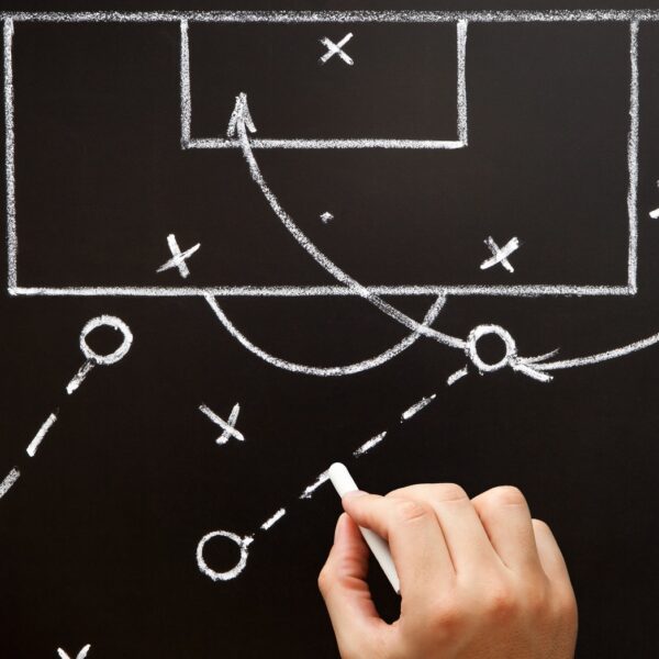 A hand with a piece of chalk drawing a diagram for a planned play in soccer.