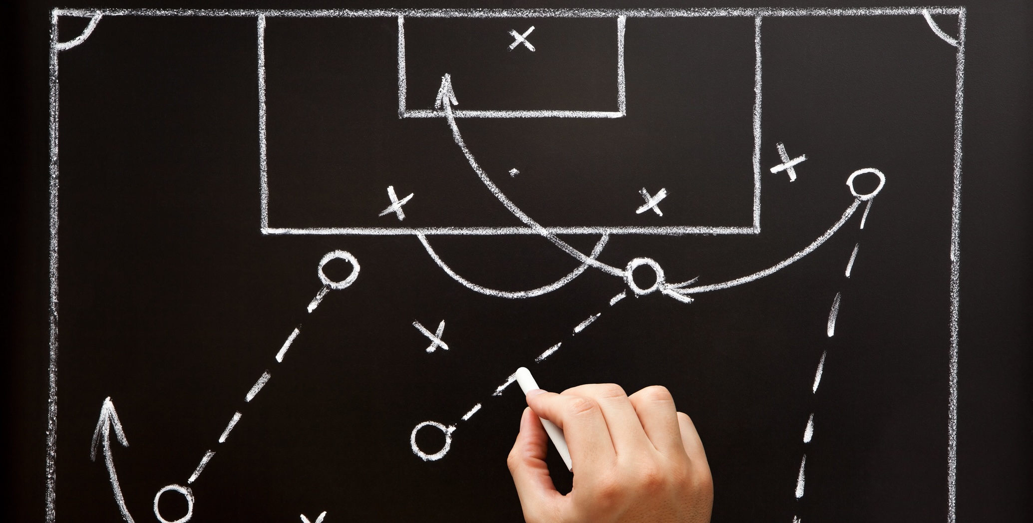 A hand with a piece of chalk drawing a diagram for a planned play in soccer.